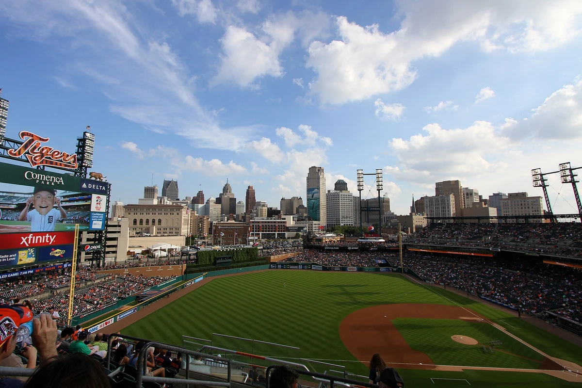 Comerica Park, Detroit, MI — Tigers signage visible in upper deck with the Detroit skyline across the outfield under a partly cloudy sky.